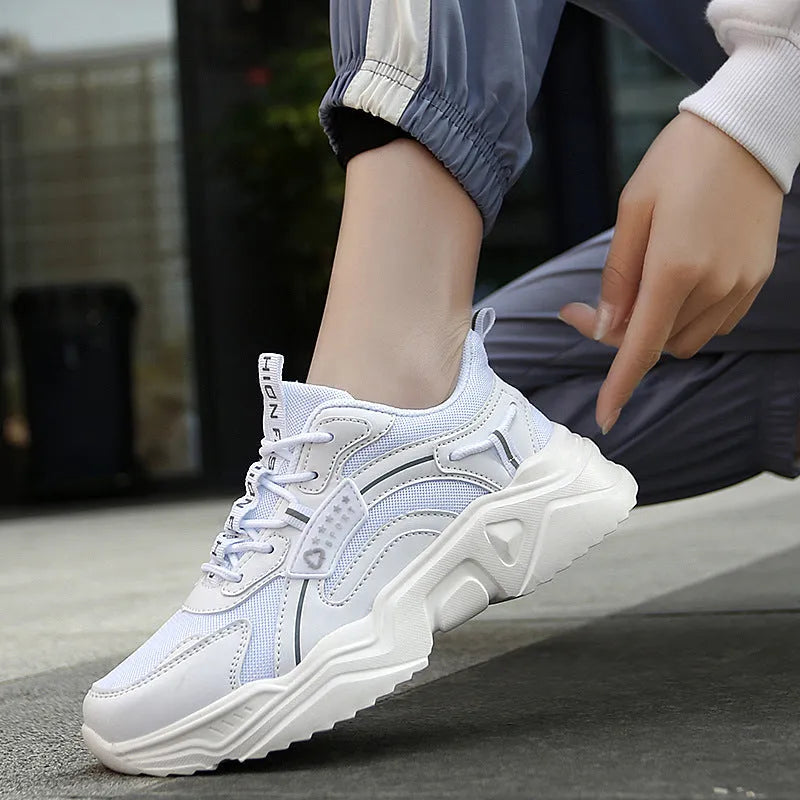 Women's white thick-soled casual sneakers with mesh upper and buckle detail on a light background.