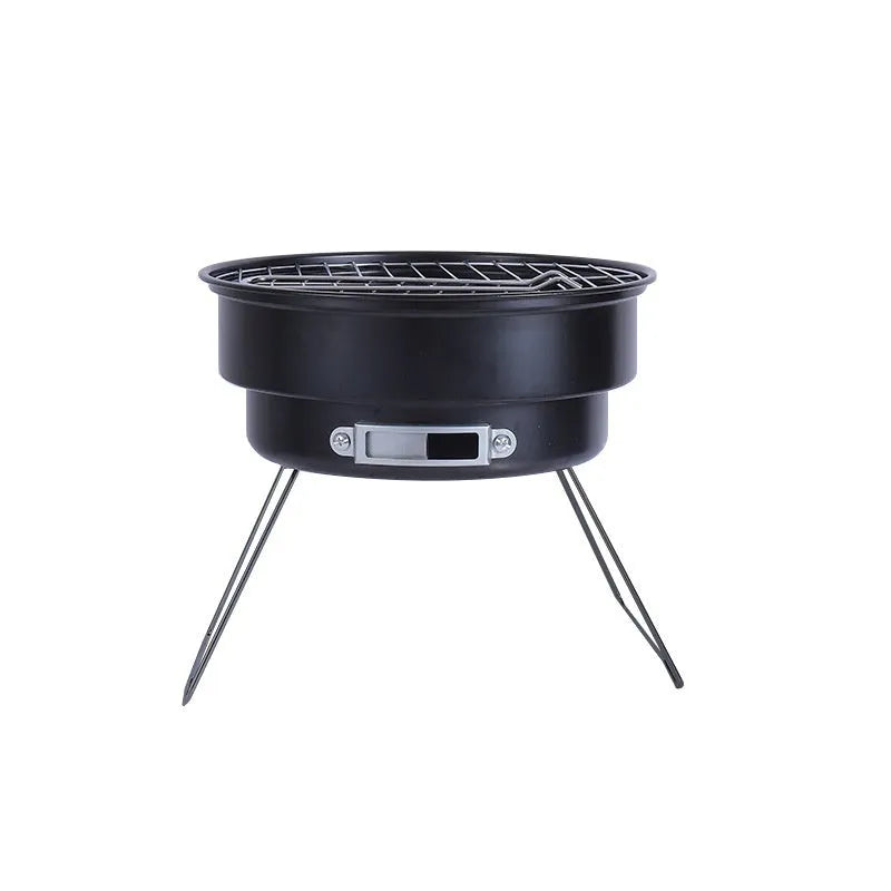 Small metal folding outdoor charcoal stove with mesh grill and tripod legs set up on grass.