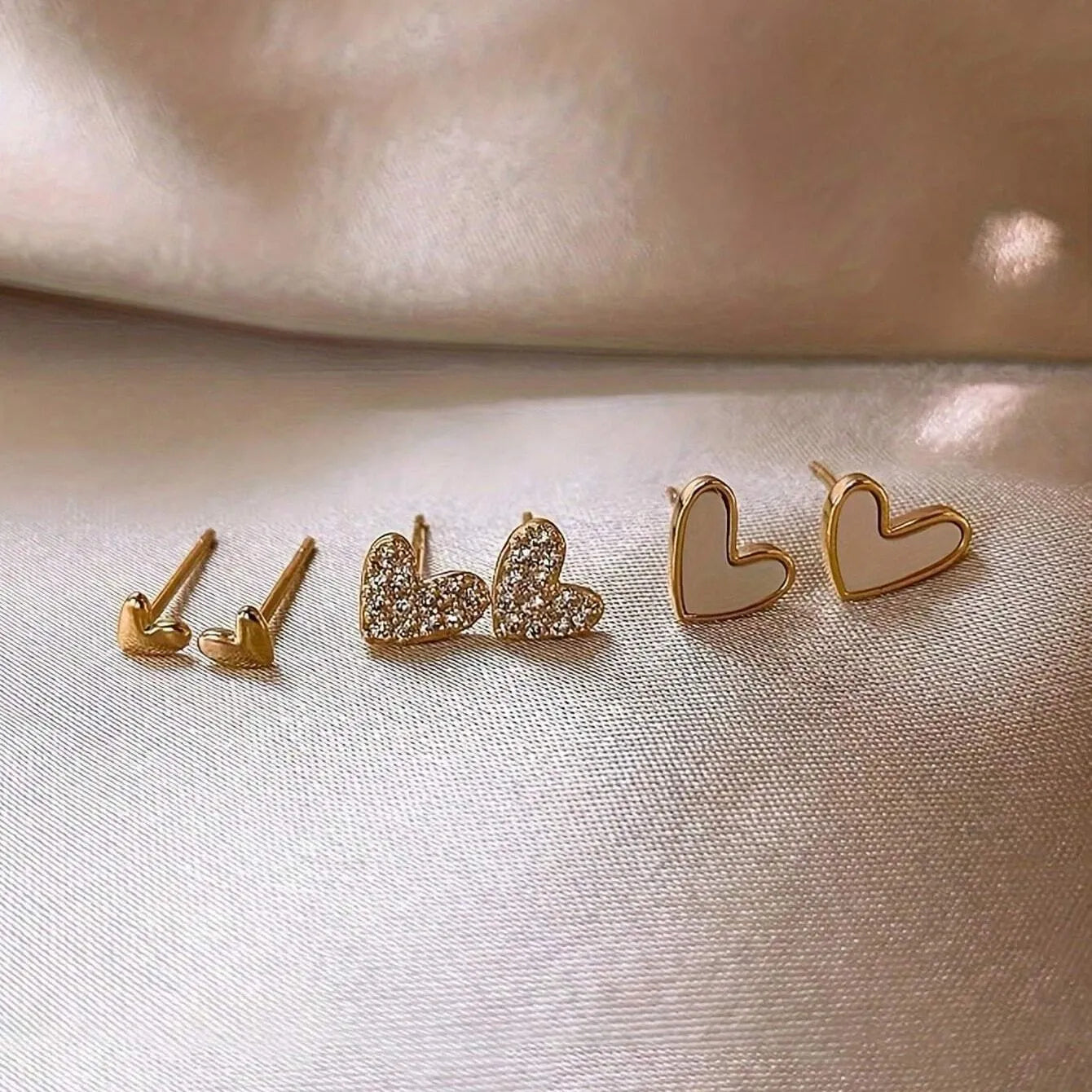 Three pairs of heart-shaped earrings with electroplated alloy construction in gold, black, pink and black-white colours