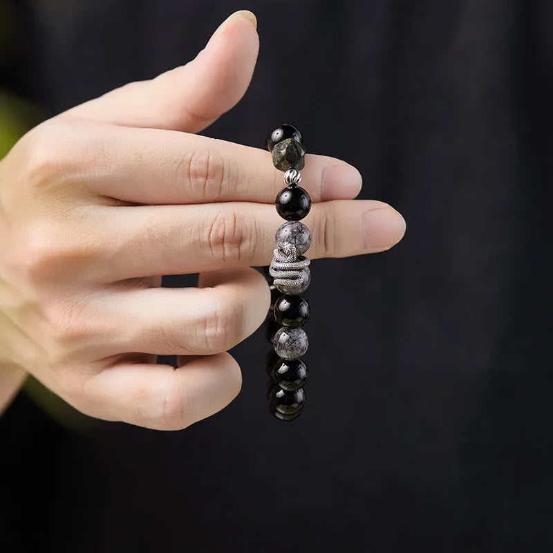 Men's obsidian black snake bracelet made of sterling silver with retro zodiac styling on a wrist.