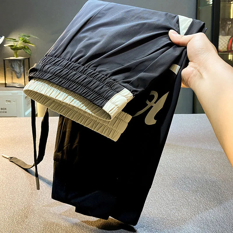 Men's solid black cotton cropped trousers with elasticated ankle band cuffs laid flat.