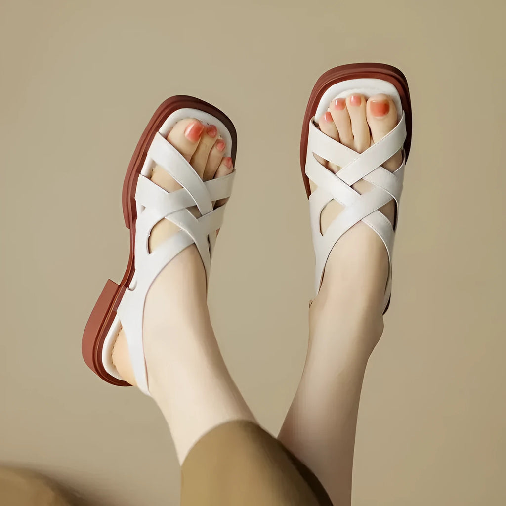 Women's black patent leather square toe sandals with cross strap design on a beach background