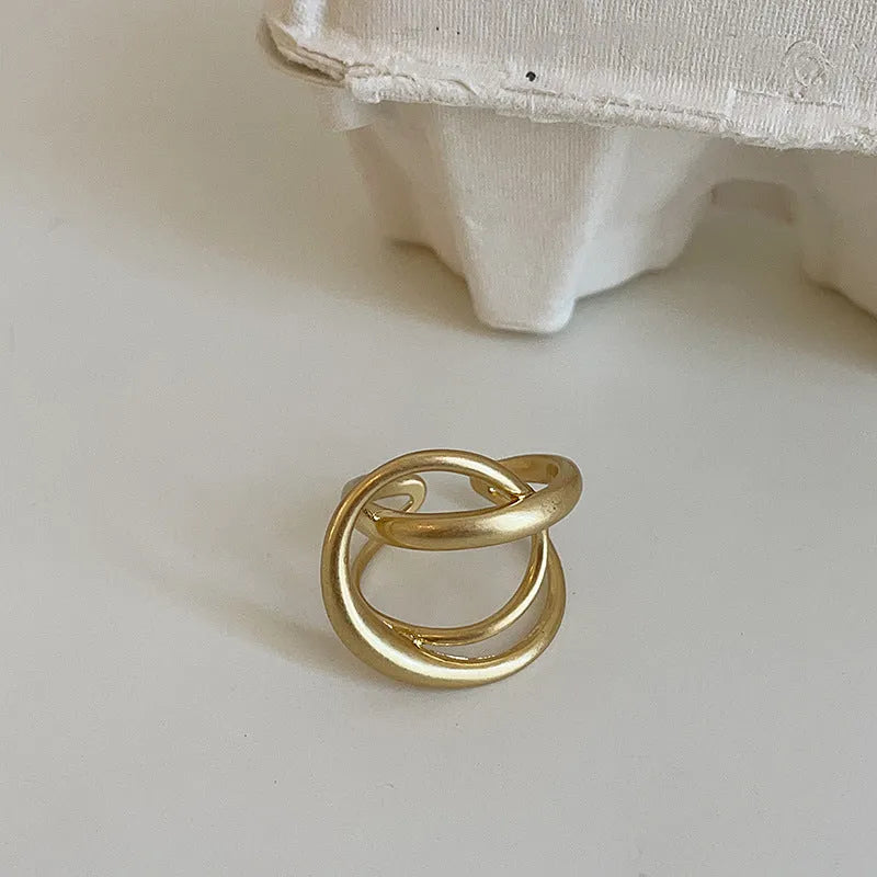 Geometric interlaced open ring with a matte metal finish in gold tone plating.
