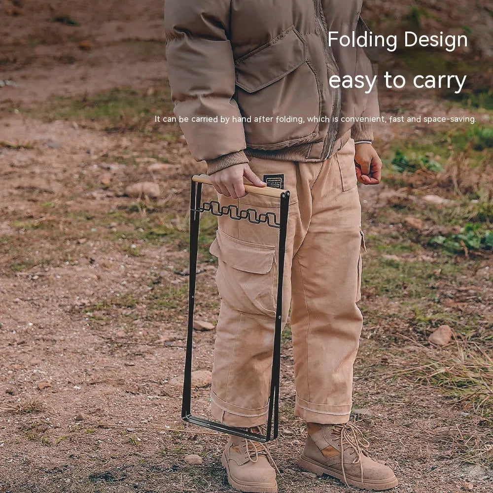 Folding black outdoor trash bag hanger with wooden carry handle on a patio.