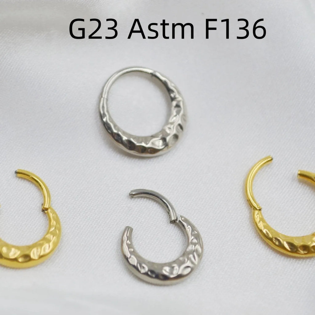 Close-up of a concave-convex titanium nose ring in gold finish on a grey background.