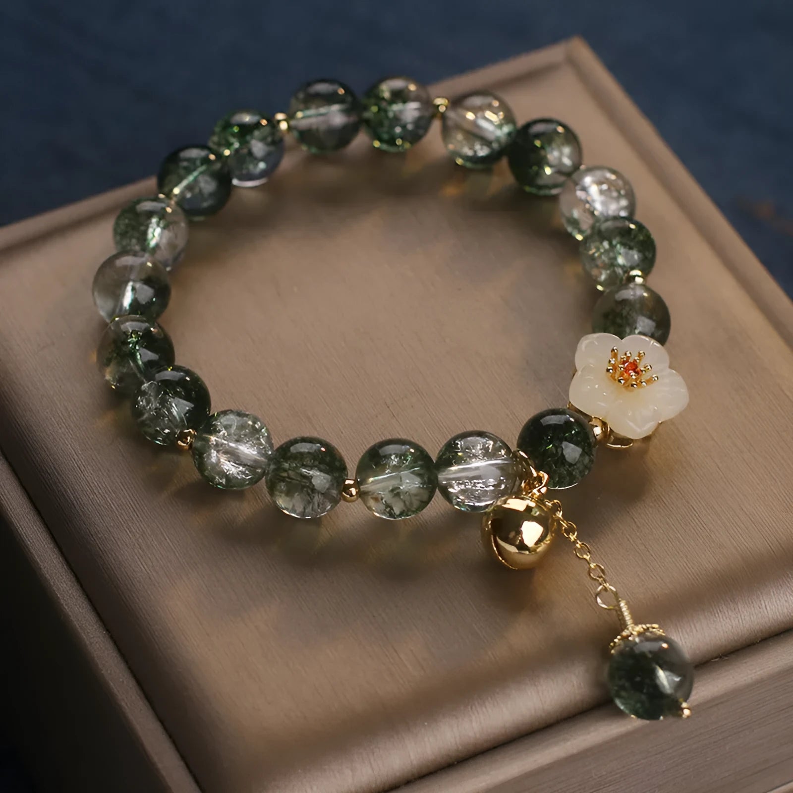 Green Phantom quartz crystal bracelet with white jade flower on a plain background