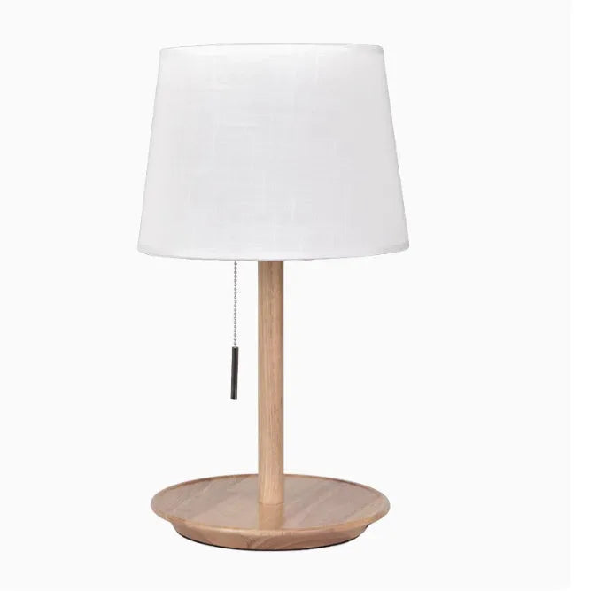 Walnut colour solid wood bedside lamp with white cloth shade on a wooden table.
