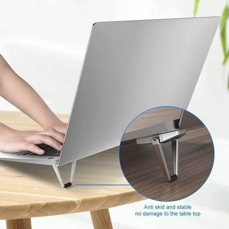 Compact silver aluminium folding laptop stand on a desk next to a wireless keyboard.