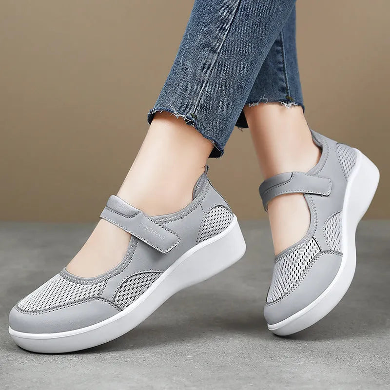 Women's grey casual slip-on shoe with mesh upper and Velcro strap on a flat sole.