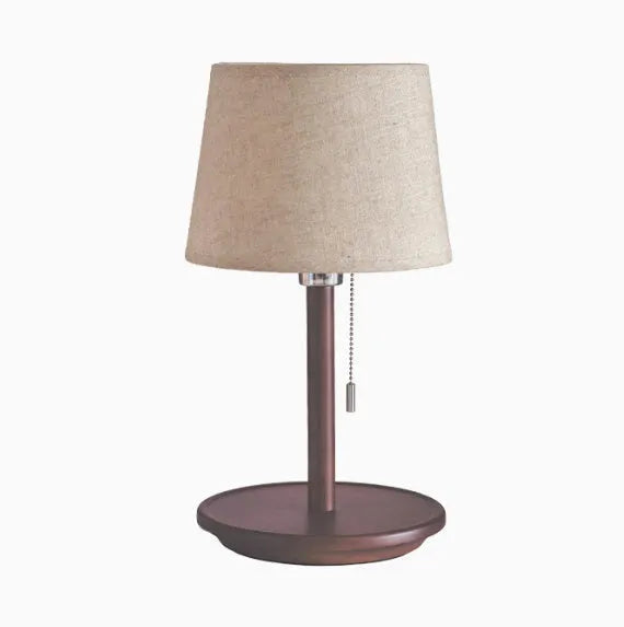 Walnut colour solid wood bedside lamp with white cloth shade on a wooden table.