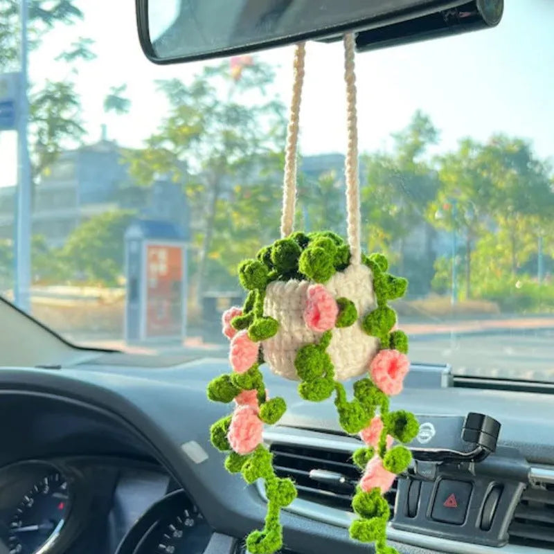 Green and white knitted wool car plant decoration with hanging rope on a car dashboard