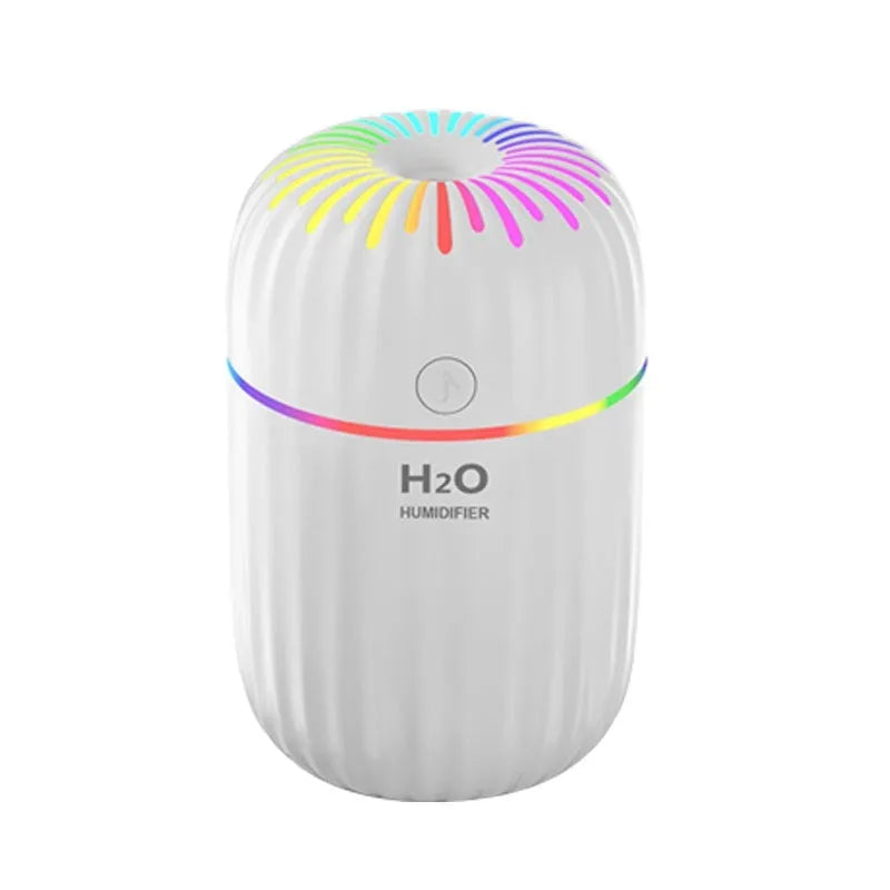 White USB personal mini humidifier with fireworks design on a wooden desk next to a laptop.