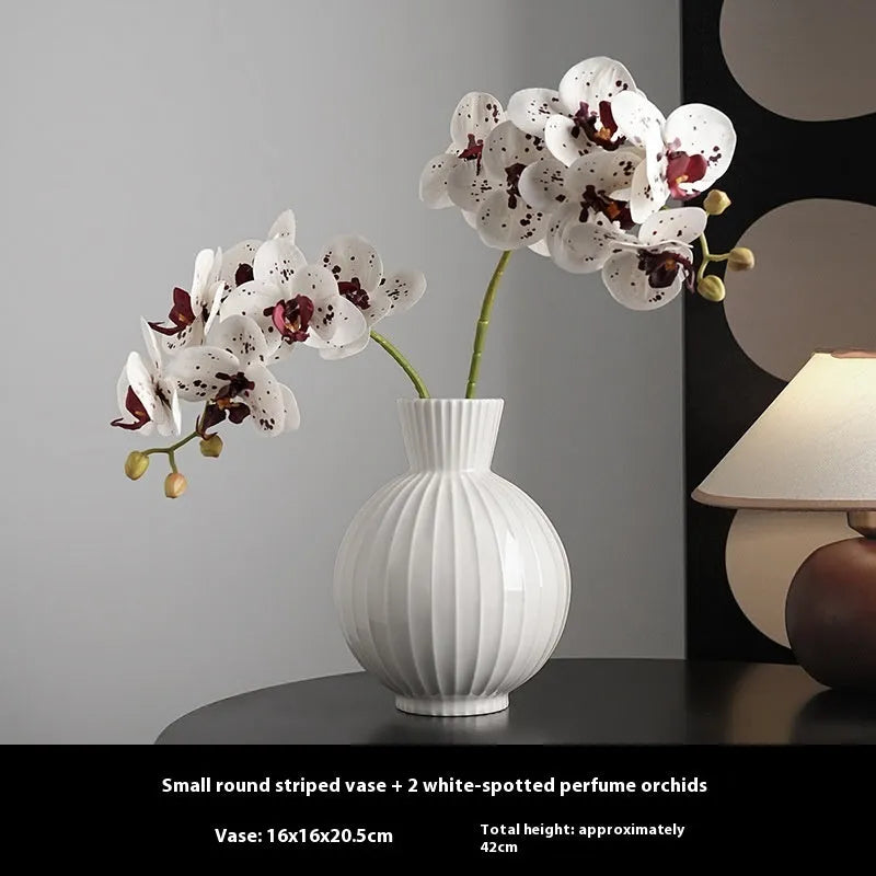 White ceramic ball vase with blue stripes and artificial blue orchid flowers on a wooden table.
