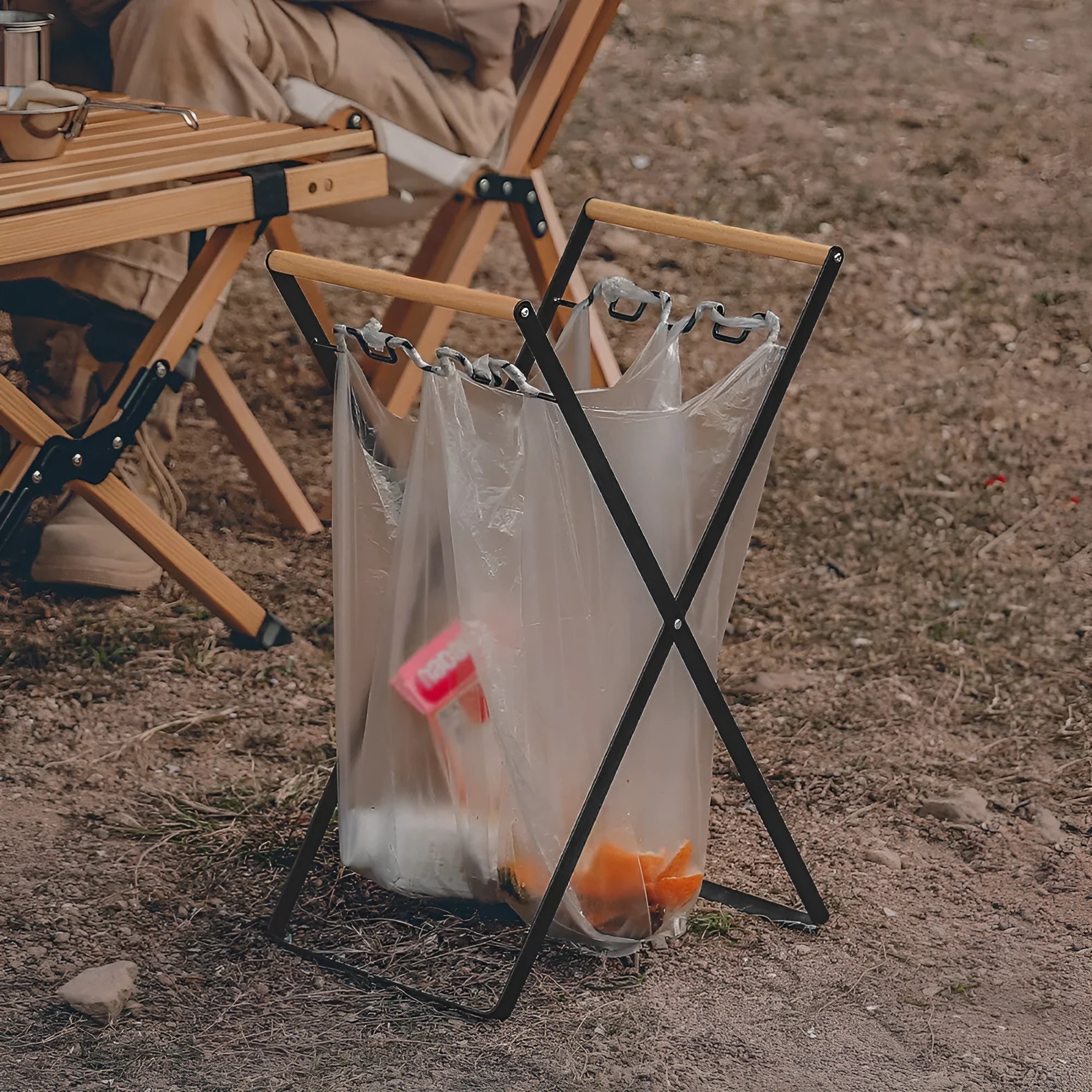 Folding black outdoor trash bag hanger with wooden carry handle on a patio.