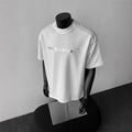 Men's loose fit cotton t-shirt with short sleeves and a printed letter design in light grey.