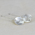 Glossy round silver women's earrings with a detailed bird, flower, and leaf design.