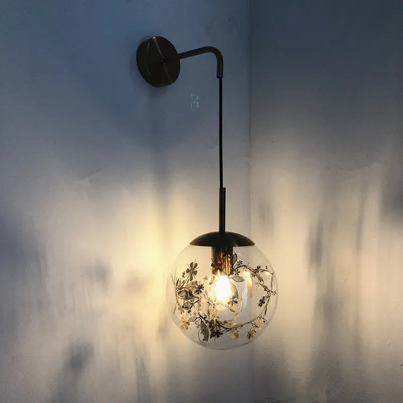 Modern minimalist glass wall lamp with golden flower finish, shown mounted beside a bed.