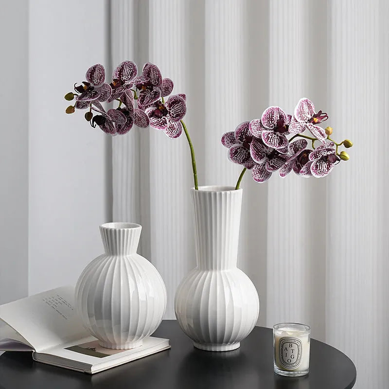 White ceramic ball vase with blue stripes and artificial blue orchid flowers on a wooden table.