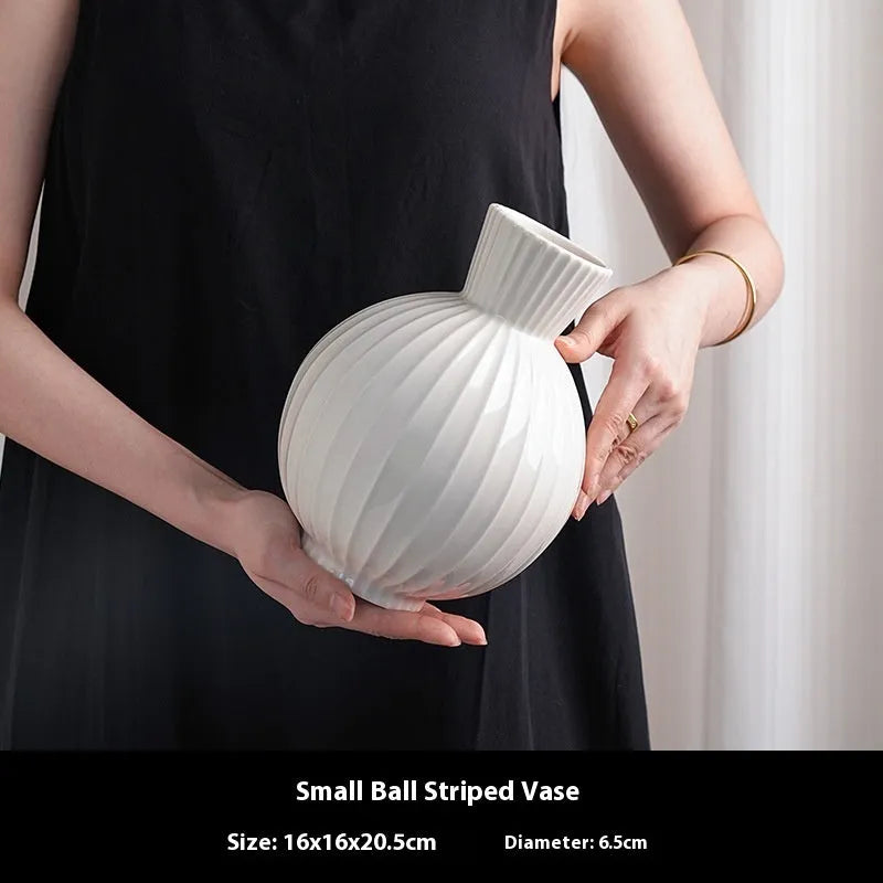 White ceramic ball vase with blue stripes and artificial blue orchid flowers on a wooden table.