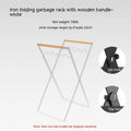 Folding black outdoor trash bag hanger with wooden carry handle on a patio.