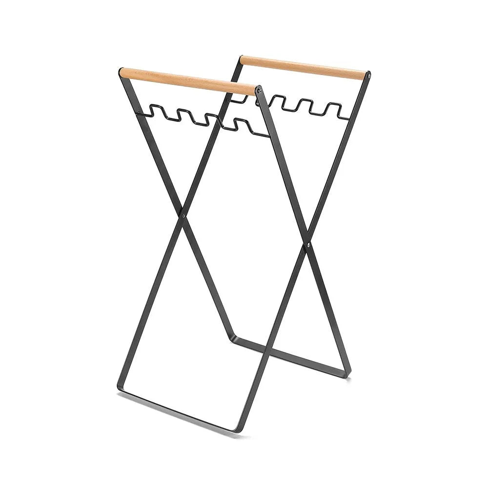 Folding black outdoor trash bag hanger with wooden carry handle on a patio.
