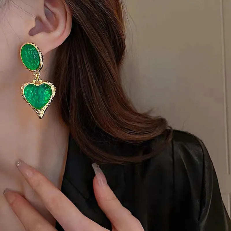A pair of oval-shaped, pleated love heart stud earrings in alloy, shown in various colours.