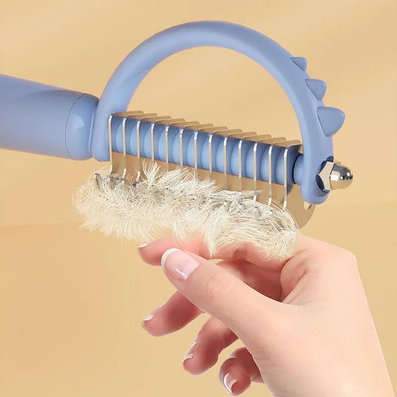 Blue dinosaur-shaped self-cleaning cat brush with double-sided stainless steel slicker pins.