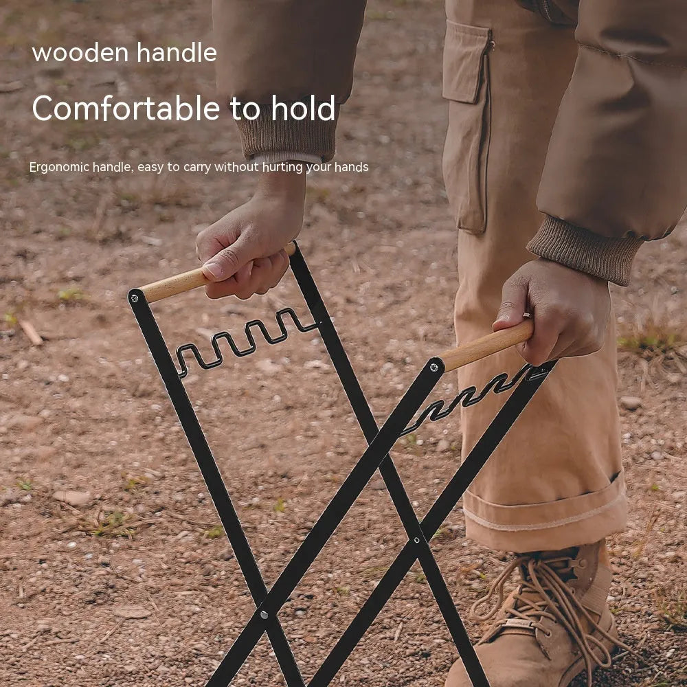 Folding black outdoor trash bag hanger with wooden carry handle on a patio.