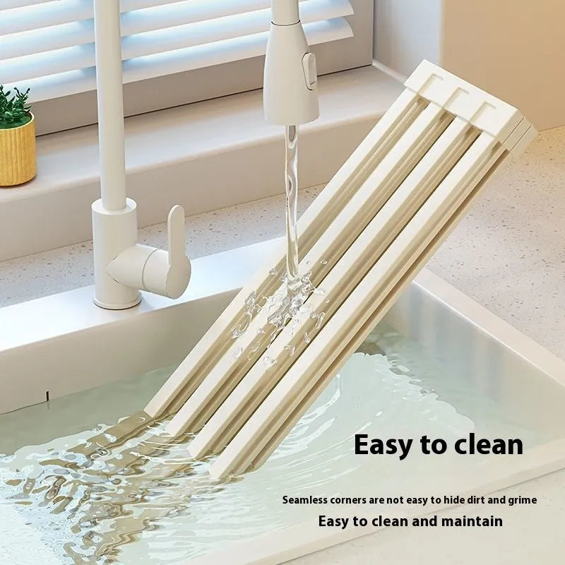 A milky white foldable stainless steel kitchen draining rack shown open on a countertop next to a sink.