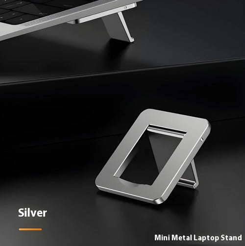 Compact silver aluminium folding laptop stand on a desk next to a wireless keyboard.