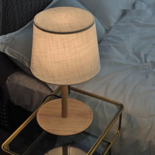 Walnut colour solid wood bedside lamp with white cloth shade on a wooden table.