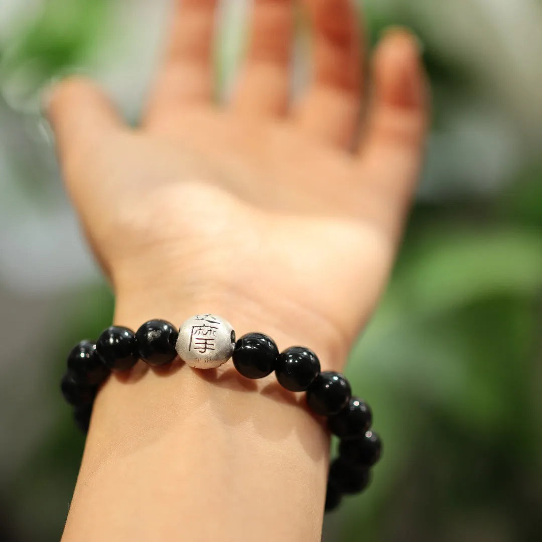 Close-up of a bracelet with large round black agate beads and a sterling silver clasp on a wrist.