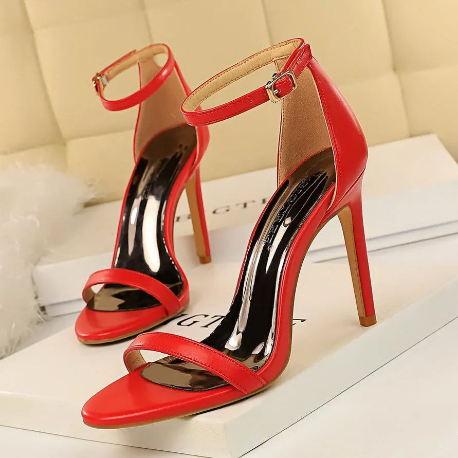 Women's white open-toe high heel sandals with an ankle buckle strap on a plain background.