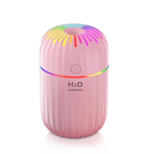 White USB personal mini humidifier with fireworks design on a wooden desk next to a laptop.