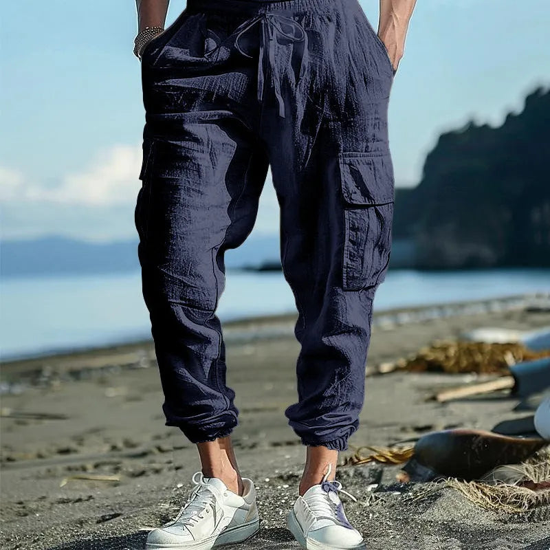 Man wearing loose-fit linen casual trousers with ankle-tied cuffs and multiple pockets in a solid colour.
