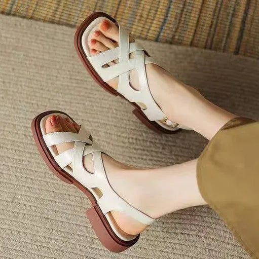 Women's black patent leather square toe sandals with cross strap design on a beach background