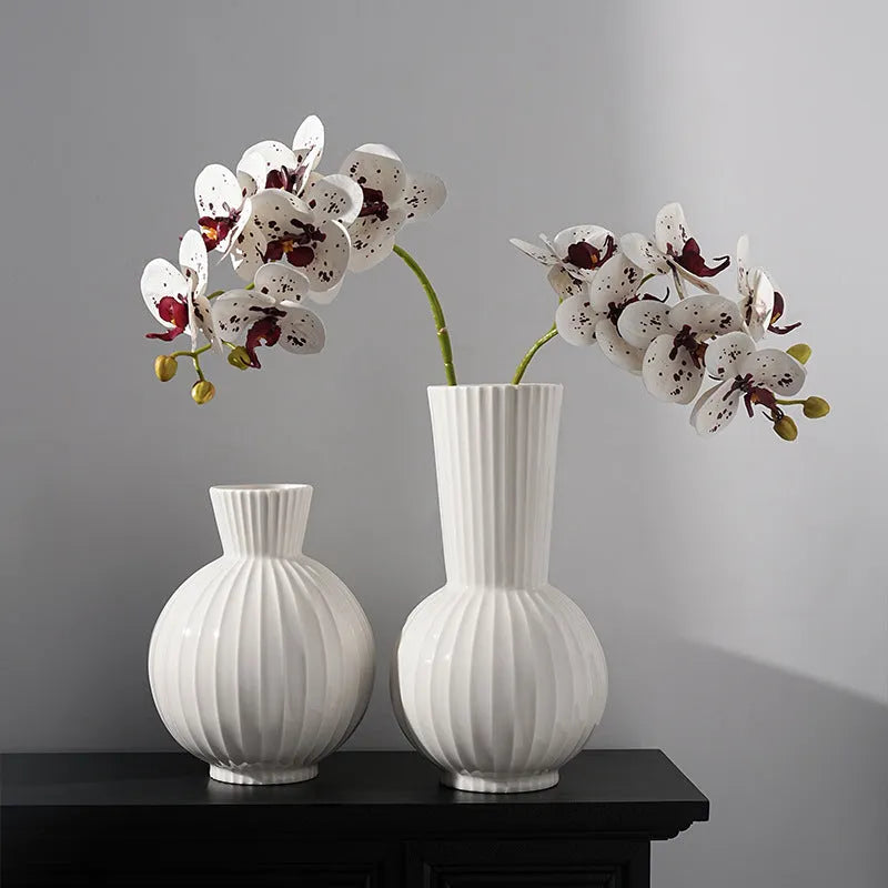 White ceramic ball vase with blue stripes and artificial blue orchid flowers on a wooden table.