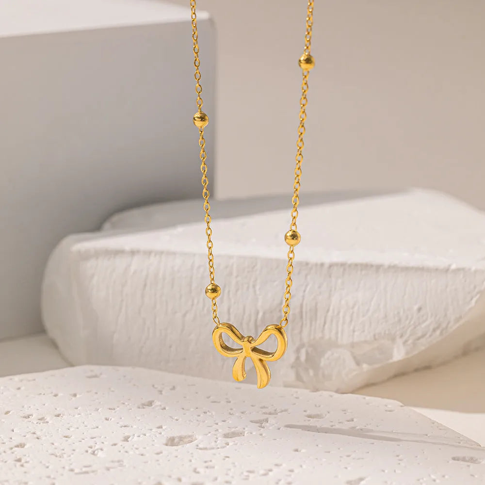 Gold electroplated bow design necklace with cross chain on white background