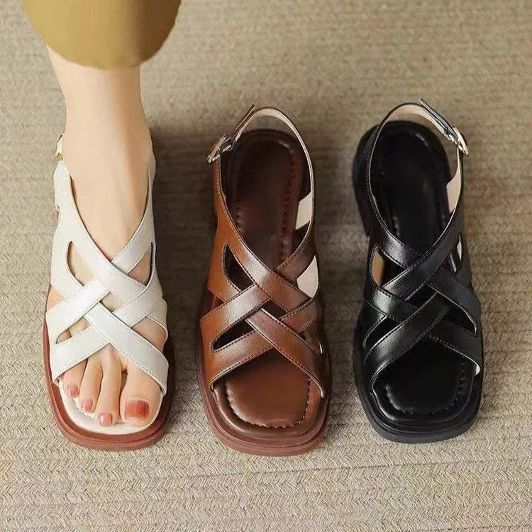 Women's black patent leather square toe sandals with cross strap design on a beach background