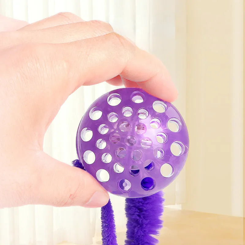 Interactive cat toy with purple bouncy ball and plush tail on wooden floor